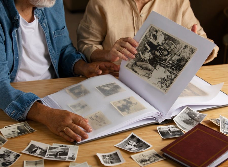 Två personer bläddrar i ett fotoalbum med svartvita fotografier på ett bord