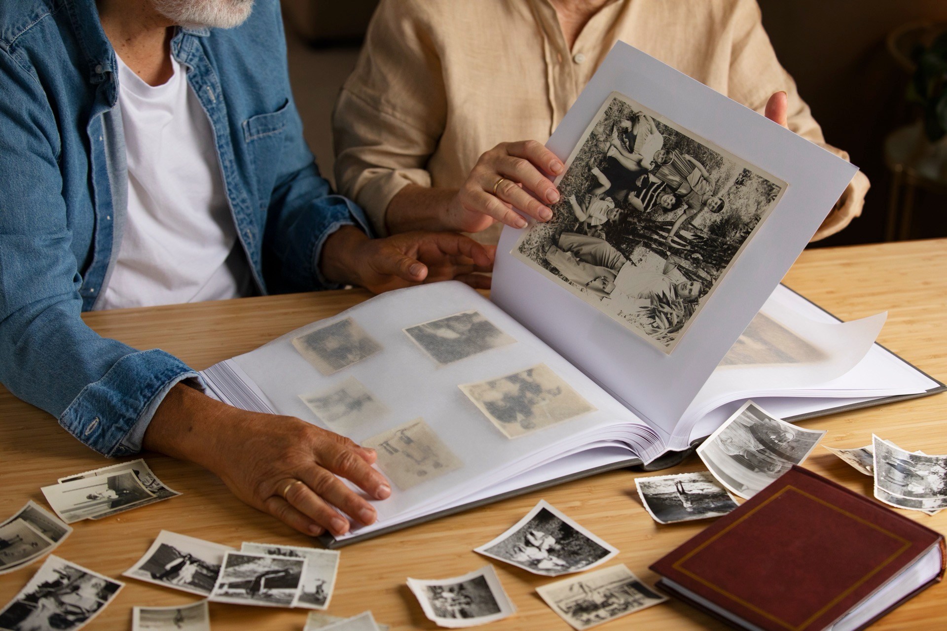 Två personer bläddrar i ett fotoalbum med svartvita fotografier på ett bord